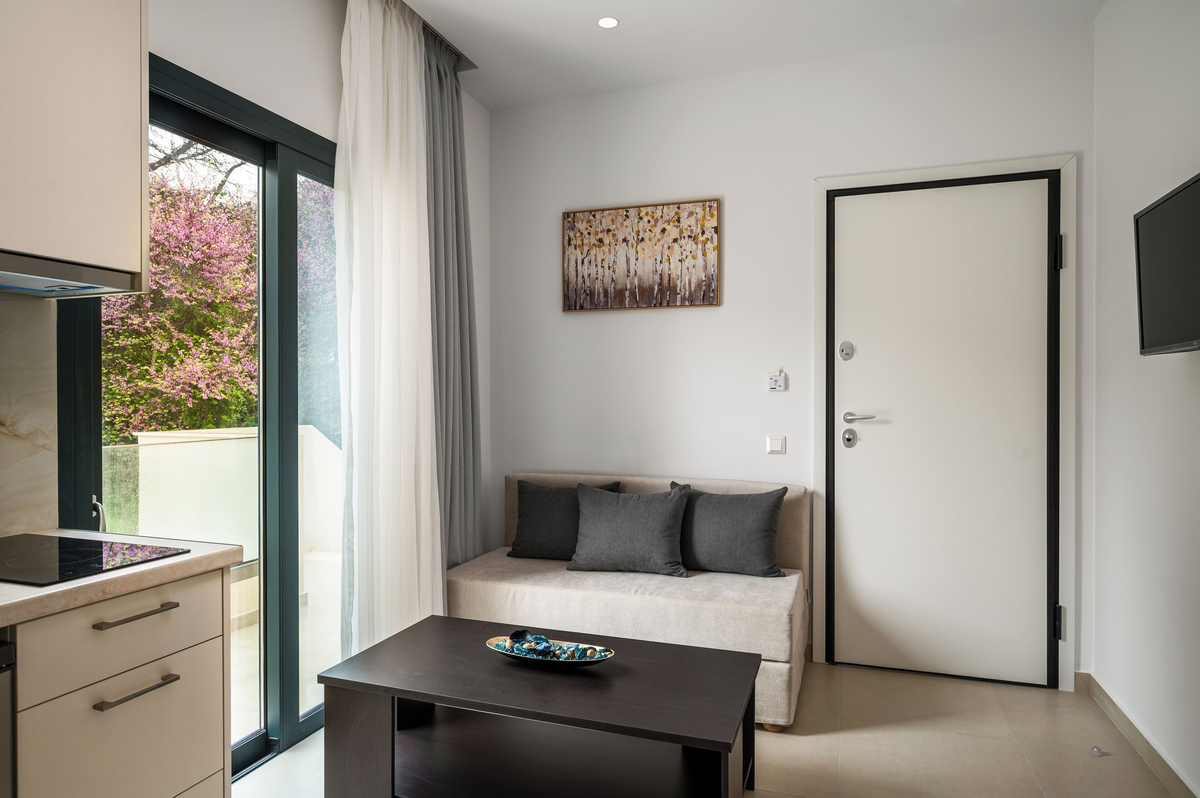 A modern room with a sofa, a dining table, a kitchen area, and a large window with curtains.