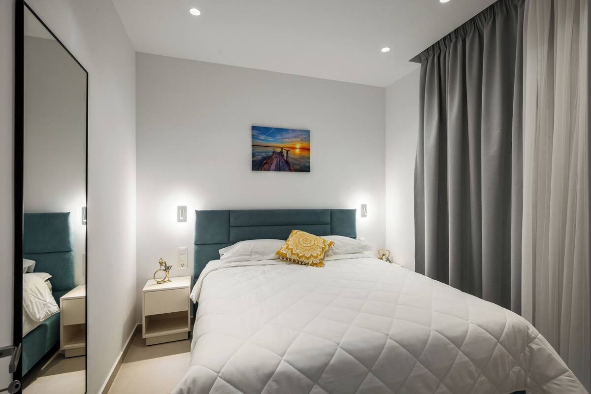 Habitació d'hotel moderna amb un llit gran, una taula de nit, un mirall i un quadre amb un paisatge de tramuntana a la paret.