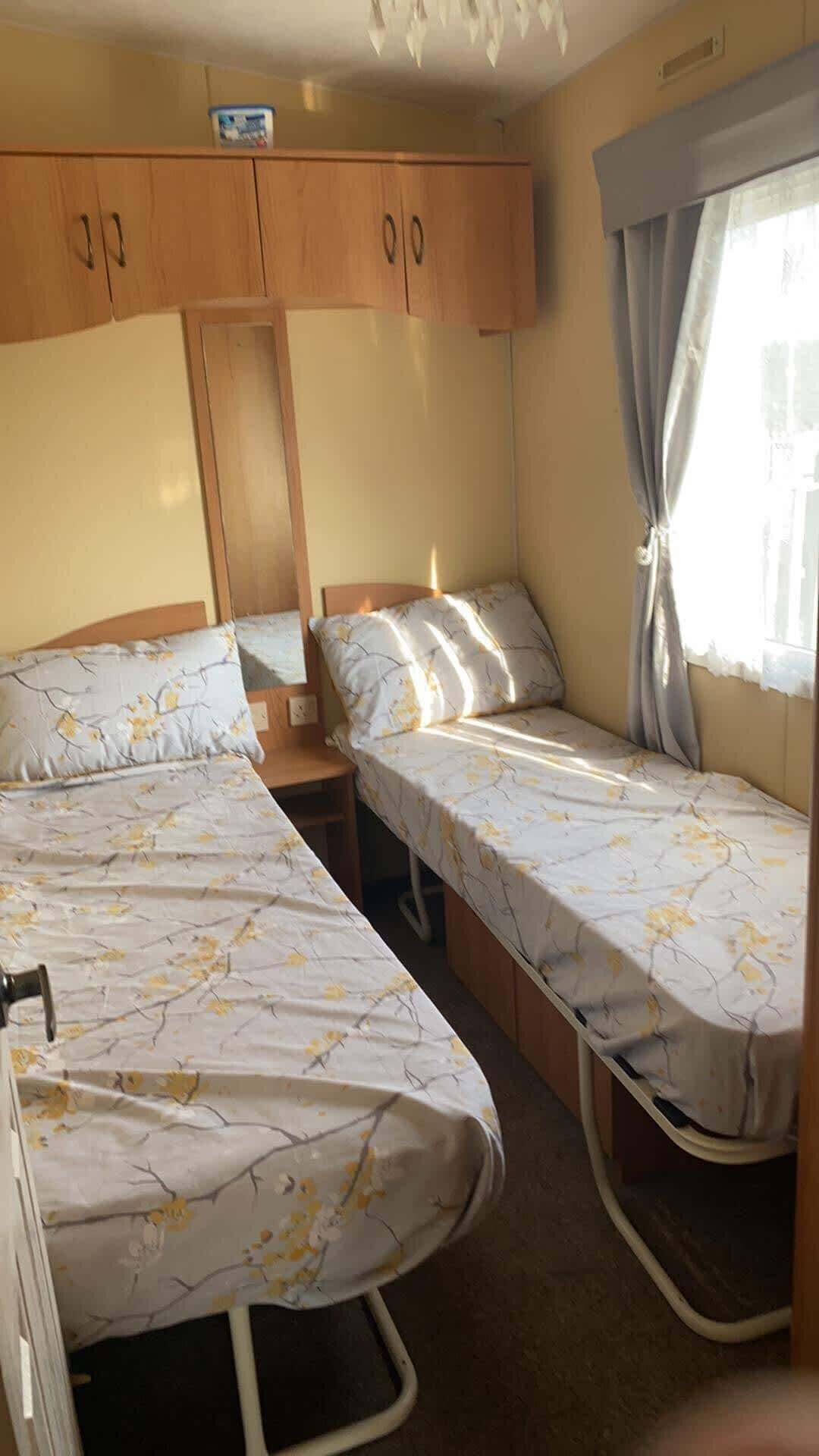 A compact room with two single beds, wooden cabinets above, and a window with curtains.