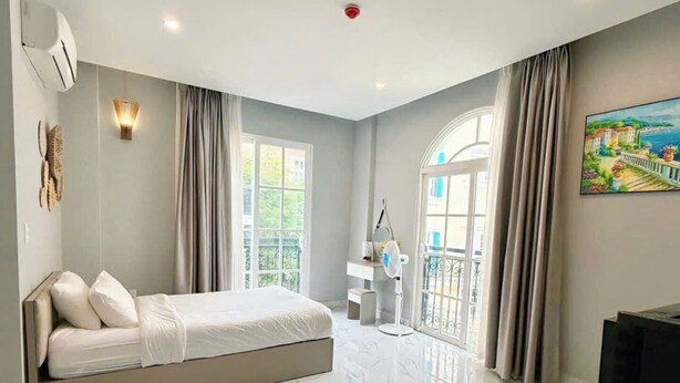 A modern bedroom with a large bed, a TV, and a painting on the wall. - Rova Hotel & Apartment - Amalfi Sunset Town (Phu Quoc)