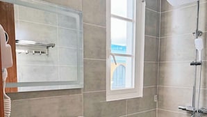 A bathroom with a large mirror, a sink, a shower, and a window. - Rova Hotel & Apartment - Amalfi Sunset Town (Phu Quoc)