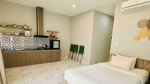 A modern bedroom with a large bed, a built-in wardrobe, a small kitchenette, and a ceiling-mounted air conditioner. - Rova Hotel & Apartment - Amalfi Sunset Town (Phu Quoc)