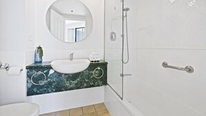 Une salle de bain moderne avec un grand miroir rond, un lavabo blanc et une douche à parois de verre.