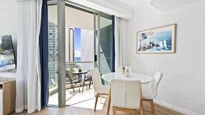 Une pièce moderne comprenant une table à manger, des chaises, un tableau et une vue sur un immeuble, visible à travers une porte vitrée.