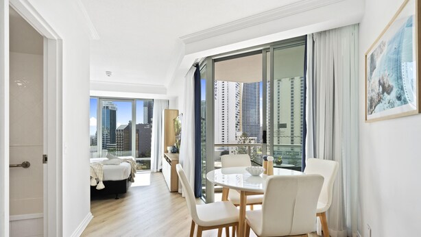 Une chambre d’hôtel moderne dotée d’un coin repas, d’une grande fenêtre offrant une vue sur la ville et d’un balcon.