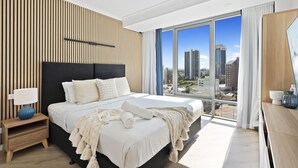 Une chambre d’hôtel moderne avec un grand lit, une table de chevet, une lampe et une vue sur la ville grâce à de grandes fenêtres.