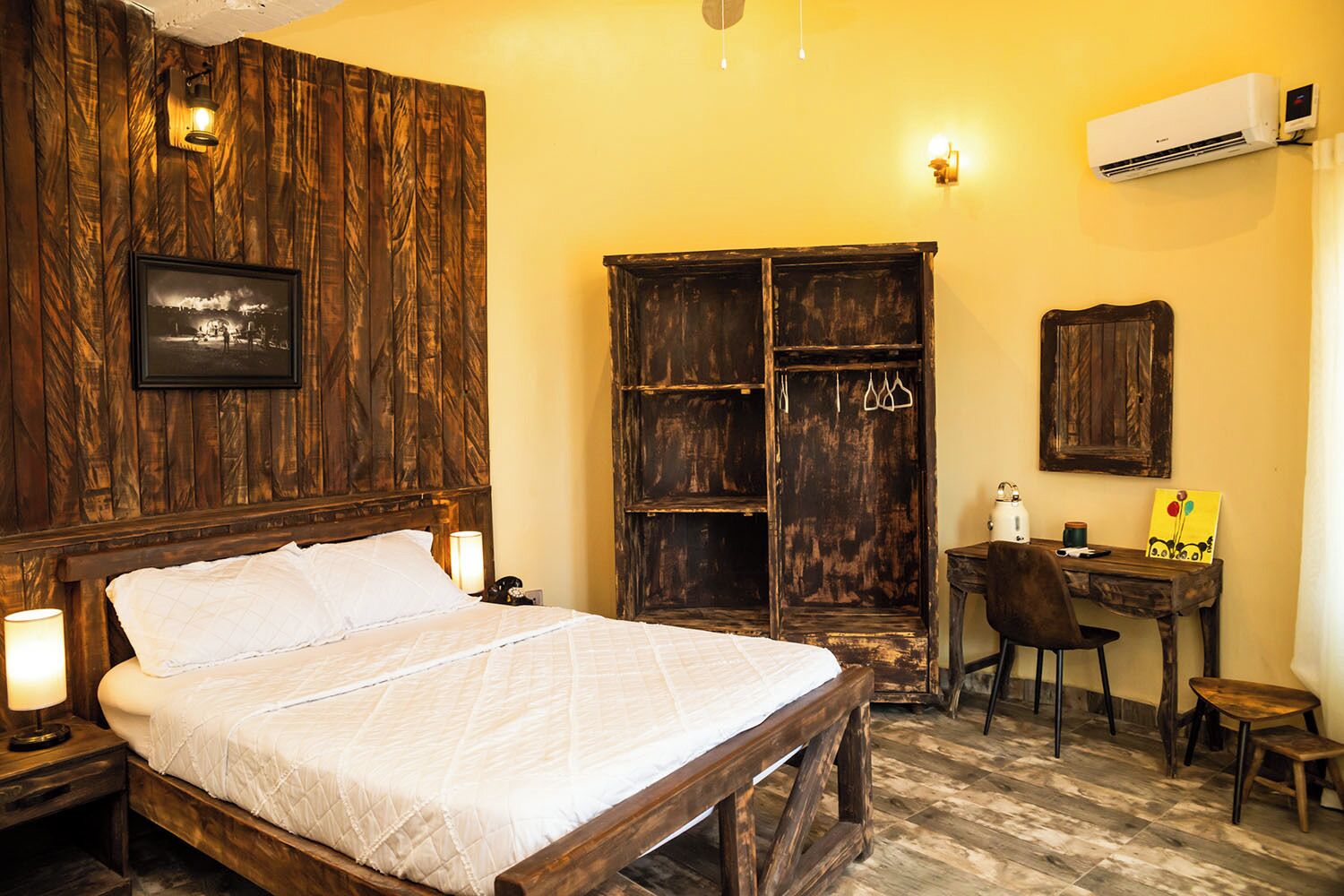 A bedroom with a wooden bed, a wardrobe, a desk with a chair, and an air conditioning unit.