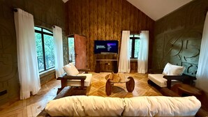 A spacious living room with a wooden floor, a large flat-screen TV mounted on the wall, and a cozy seating area with sofas and a coffee table.