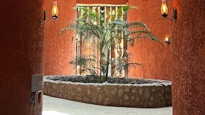 A spacious atrium with a central plant, a stone bench, and a view of a balcony with railings.