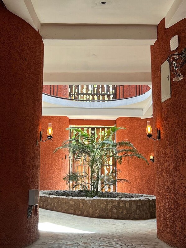 Ein geräumiges Atrium mit einer zentralen Pflanze, einer Steinsitzbank und Blick auf einen Balkon mit Geländern.