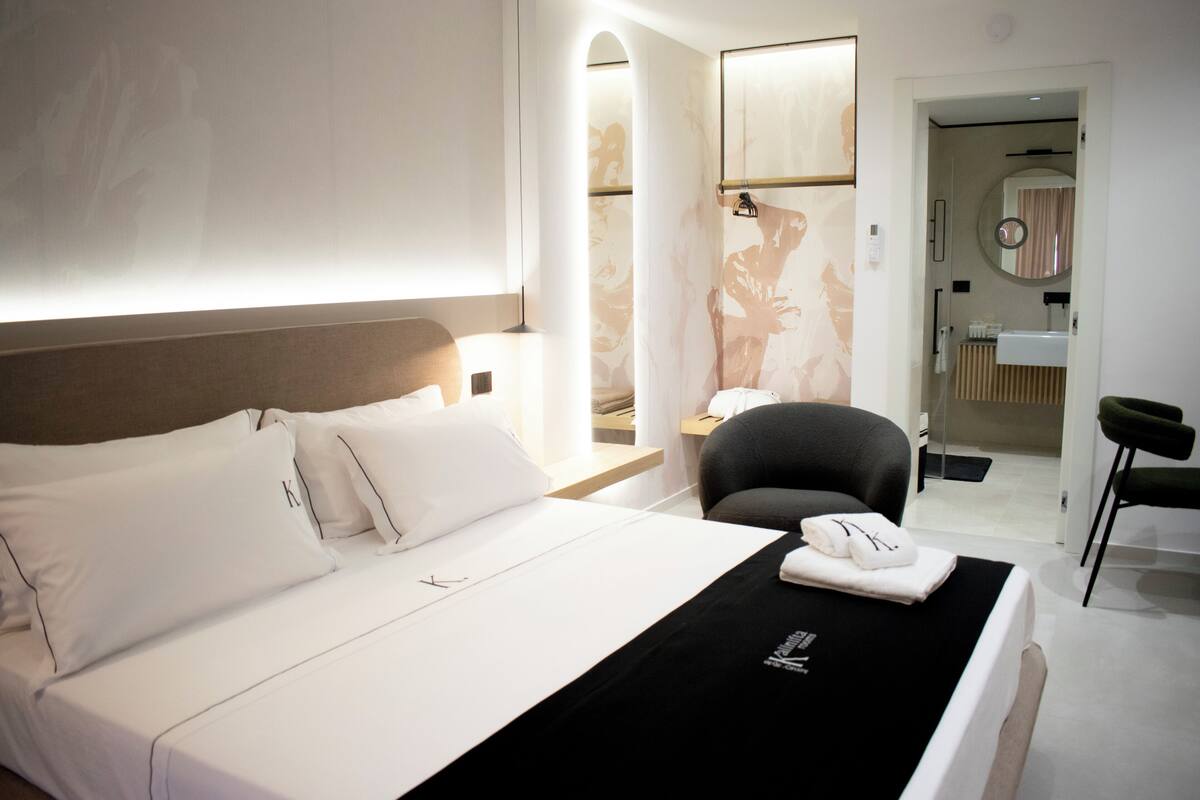 Une chambre d’hôtel moderne, dotée d’un grand lit, d’un bureau, d’une chaise et d’une salle de bain visible à travers une porte ouverte.