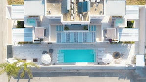 Vista aérea de un hotel moderno con una piscina central, múltiples balcones y zonas de estar al aire libre.