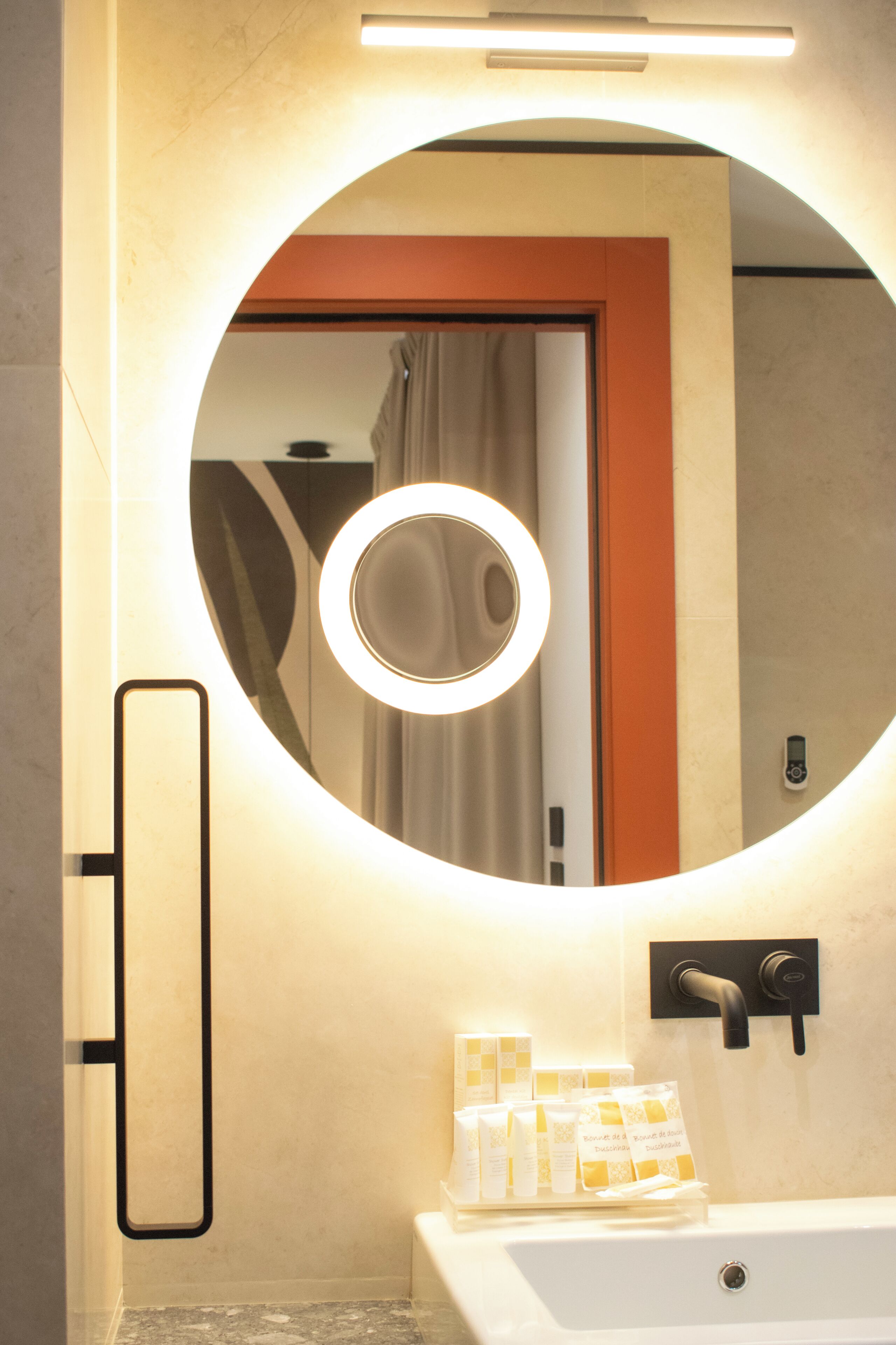 A bathroom with a circular mirror, a sink, and toiletries.