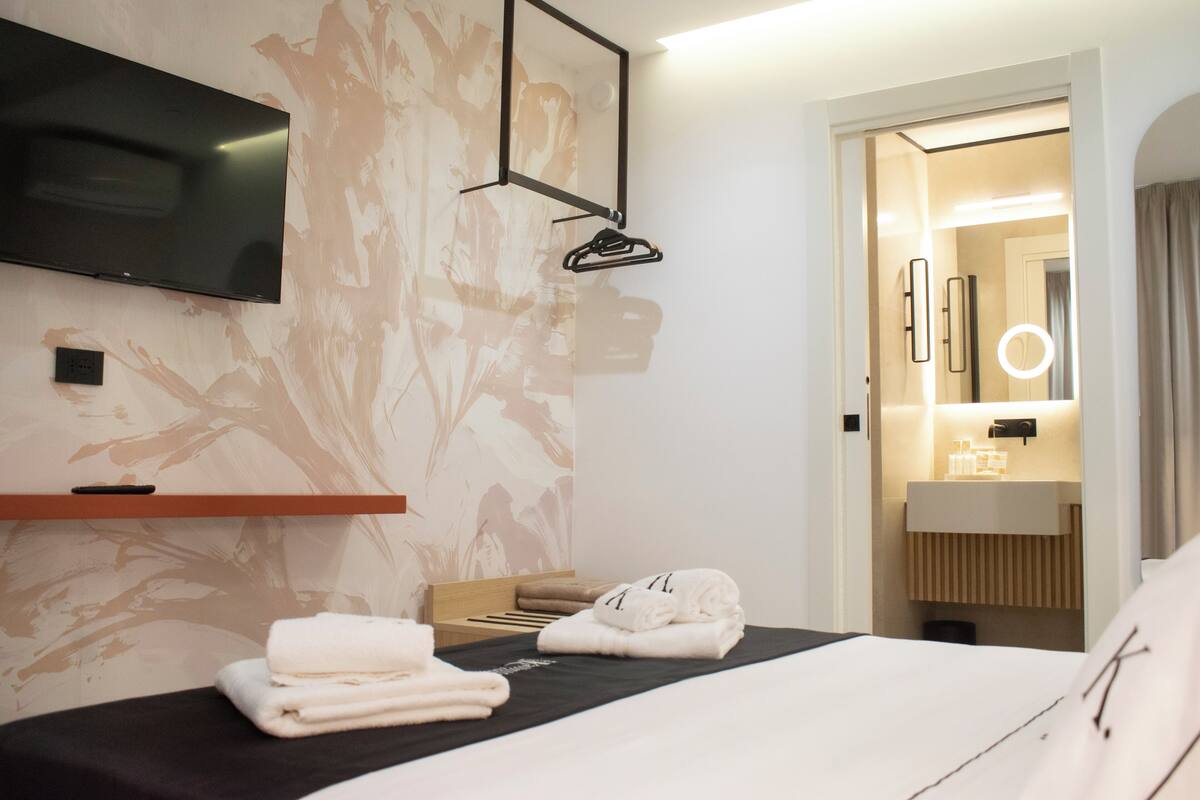Une chambre d’hôtel comprenant un lit, un téléviseur fixé au mur, un porte-serviettes et une salle de bain avec un miroir et un lavabo.