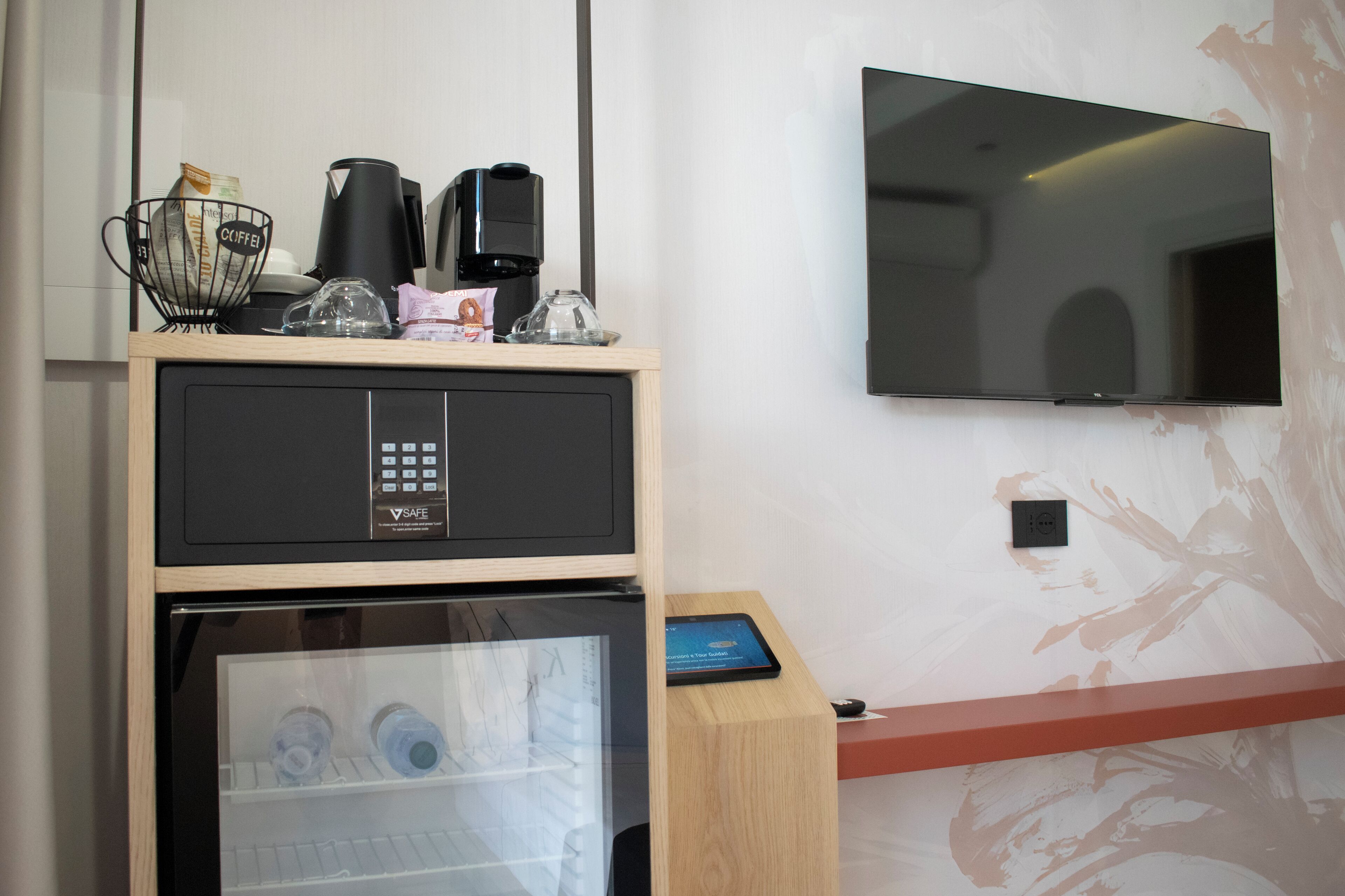 A minibar with a coffee maker, a glass container, and a tablet on a wooden counter.