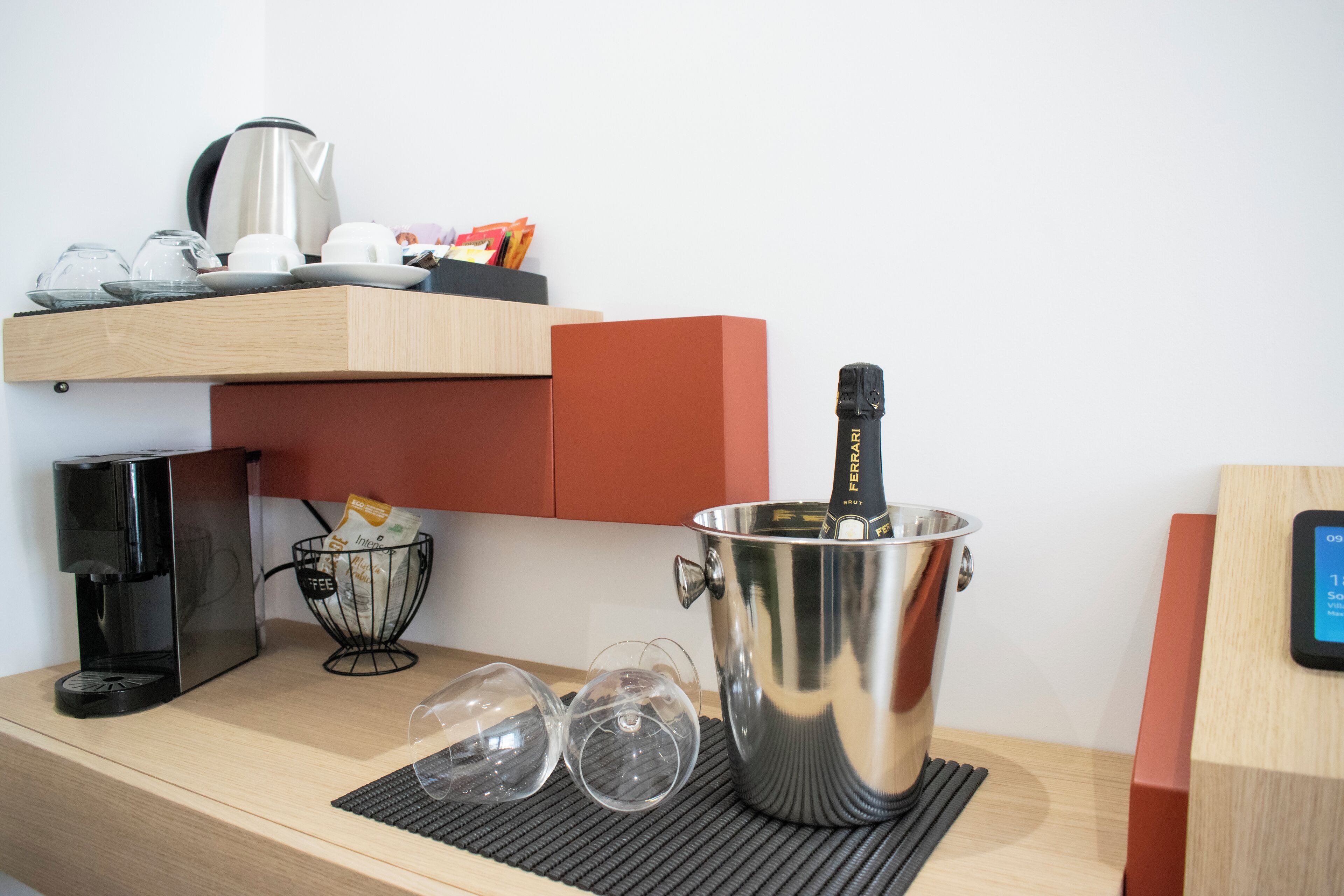 A kitchenette with a coffee maker, wine glasses, a bottle of champagne, and a kettle.
