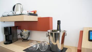 A kitchenette with a coffee maker, wine glasses, a bottle of champagne, and a kettle.