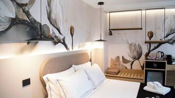 A hotel room with a bed, a nightstand, a wall-mounted shelf with a kettle, and a large abstract painting.