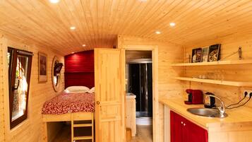 A compact wooden cabin with a single bed, a small kitchenette, and a shower.