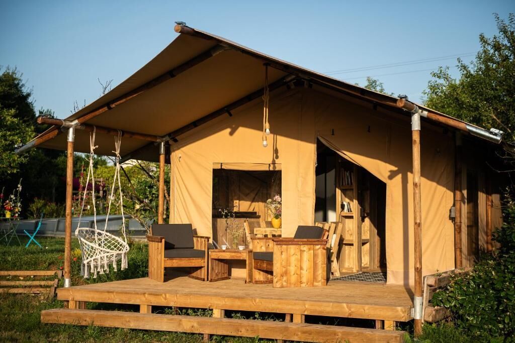 A tented accommodation with a wooden deck, seating area, and a small table.