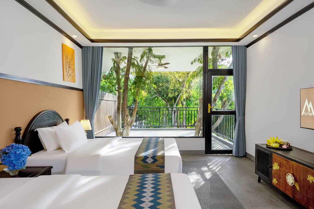 A hotel room with two beds, a balcony with a view of greenery, and a modern decor style.