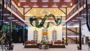 A spacious lobby with a central reception desk, a decorative dragon sculpture, and traditional blue and yellow wall decor. - Fullman Hotel (Luang Prabang)