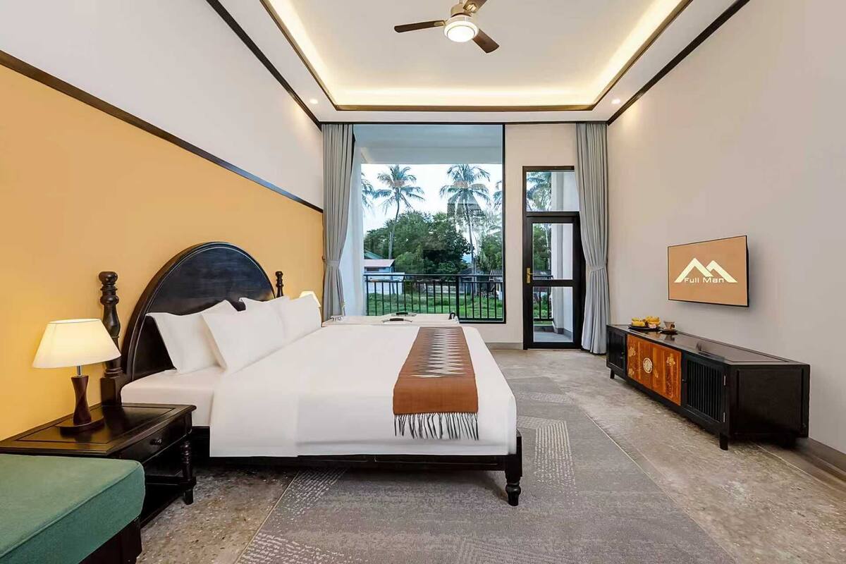 A hotel room with a bed, a nightstand, a lamp, a dresser, and a view of the outdoors.