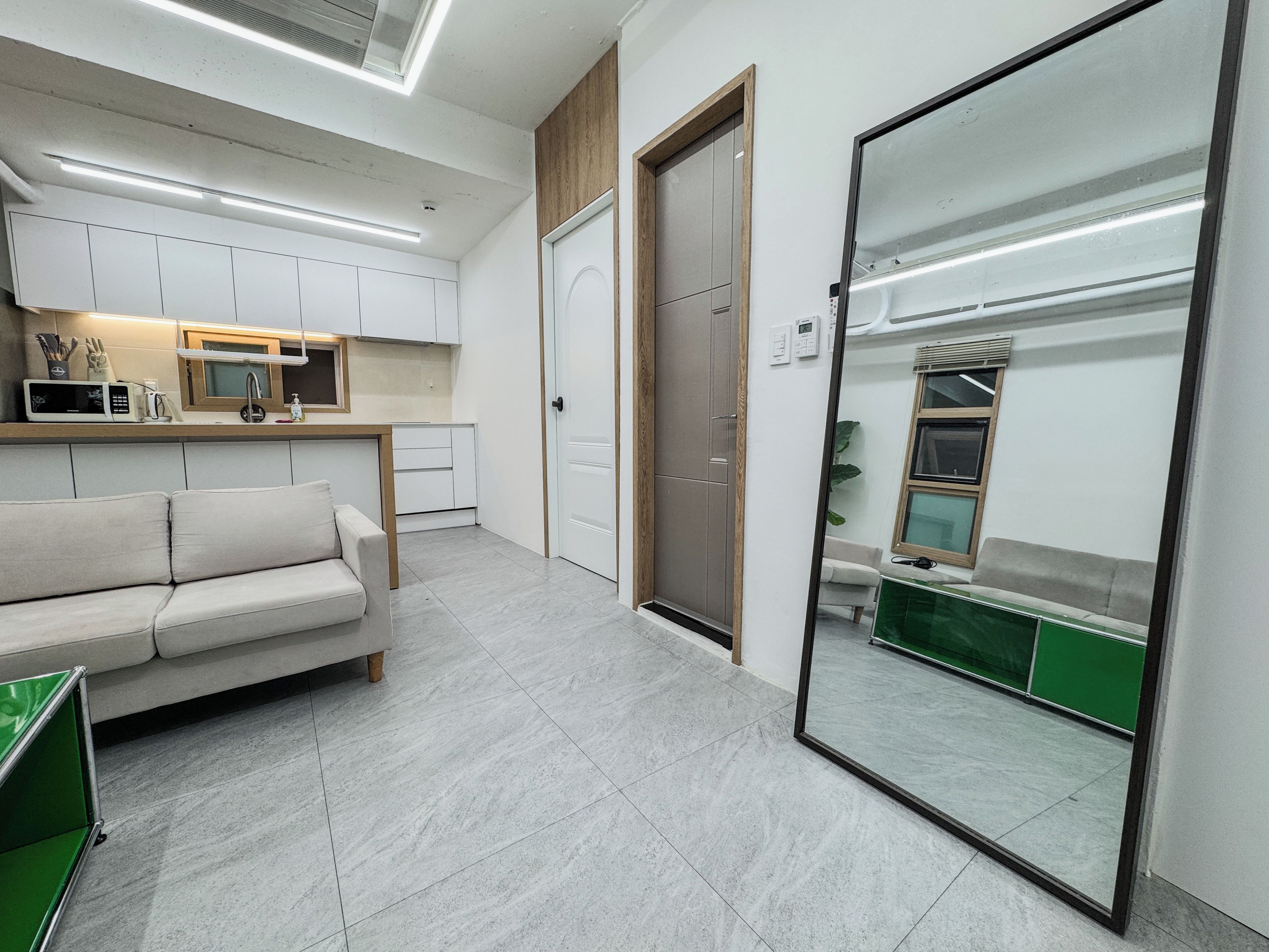 A modern interior with a kitchenette, a sofa, a door, and a large mirror.