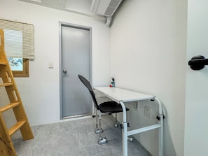 Una habitación con un escritorio blanco, una silla, una escalera de madera, una puerta y una ventana con persianas.