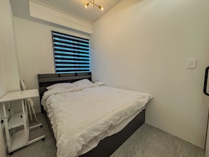 Un dormitorio con cama, mesita de noche, silla y ventana con persianas.