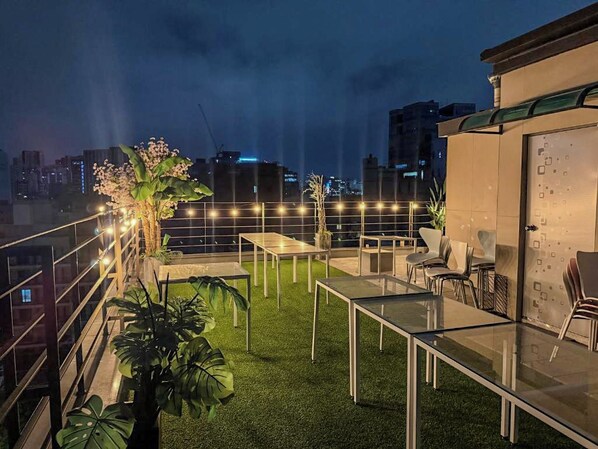 A rooftop terrace with a glass table, chairs, and potted plants.