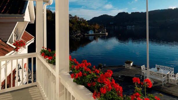 A waterfront property with a wooden dock, white railings, and red flowers. - Ramsvig Handelsstad (Stavanger)