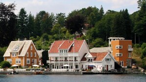 A waterfront property with a mix of traditional and modern architecture, including a prominent white building with a red roof and a smaller orange building. - Ramsvig Handelsstad (Stavanger)