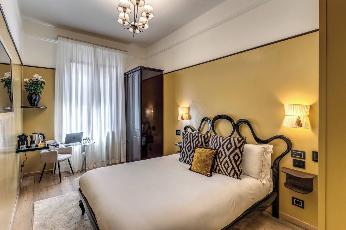 A hotel room with a bed, desk, chair, and a computer.