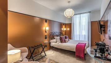 A modern hotel room with a bed, a glass side table, a chair, a lamp, and a hanging light fixture.