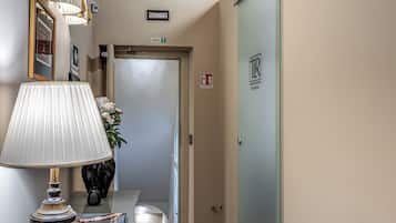 Ein Flur mit einer Lampe, einem Blumenstrauß in einer Vase, einem gerahmten Bild und einer Tür mit einem Schild.
