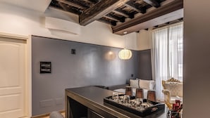 Una cocina moderna con una isla central, un área de comedor con una silla blanca tapizada y un amplio ventanal con cortinas ligeras.