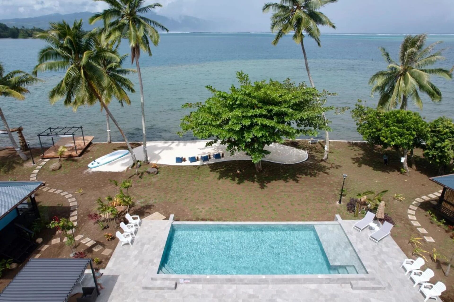 Ein Pool mit Liegestühlen, Palmen und Blick aufs Meer.