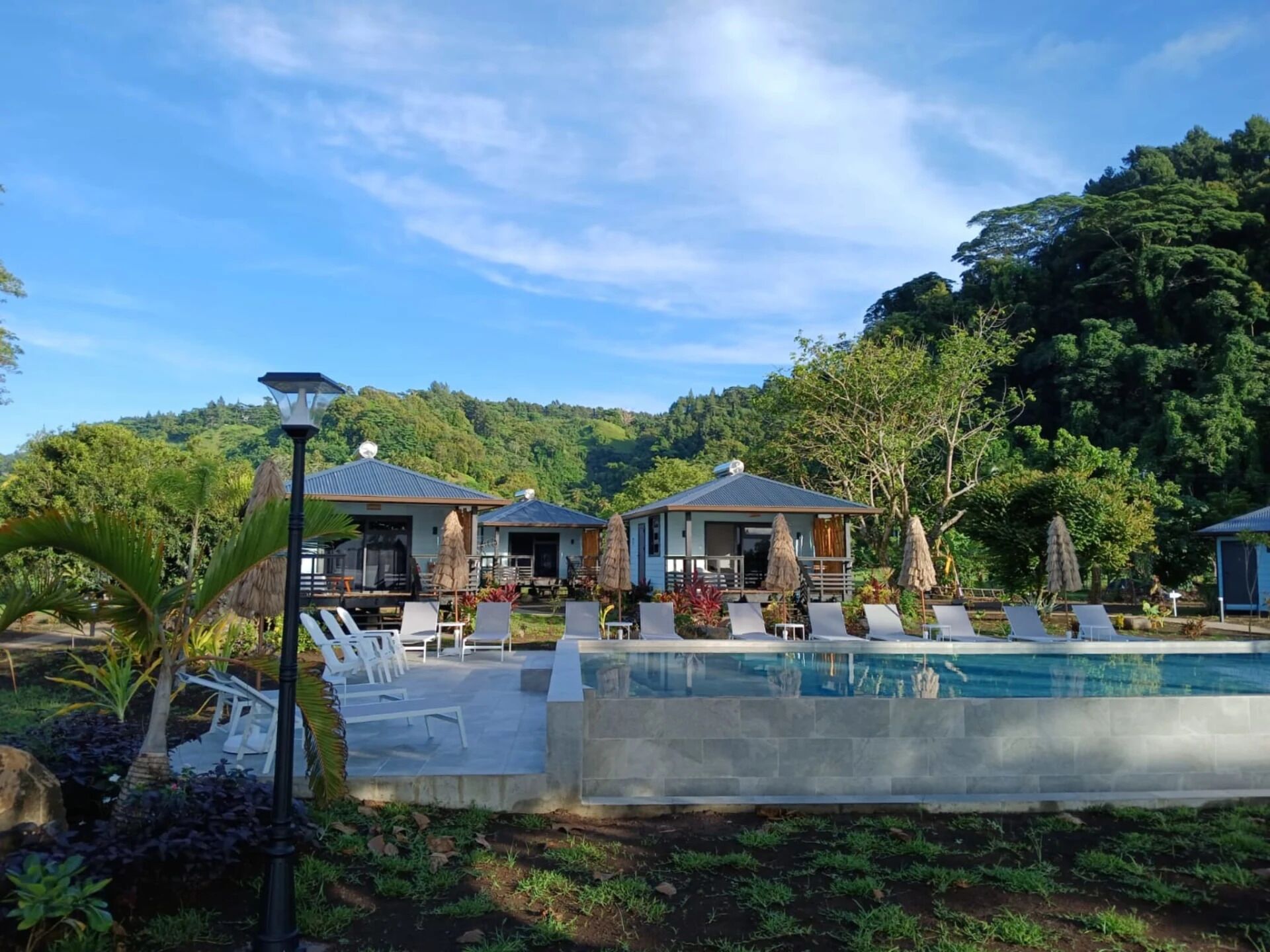 A pool area with lounge chairs and umbrellas, surrounded by lush greenery and hills.
