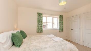 A bedroom with a bed, green pillows, a window with curtains, a radiator, and a door.