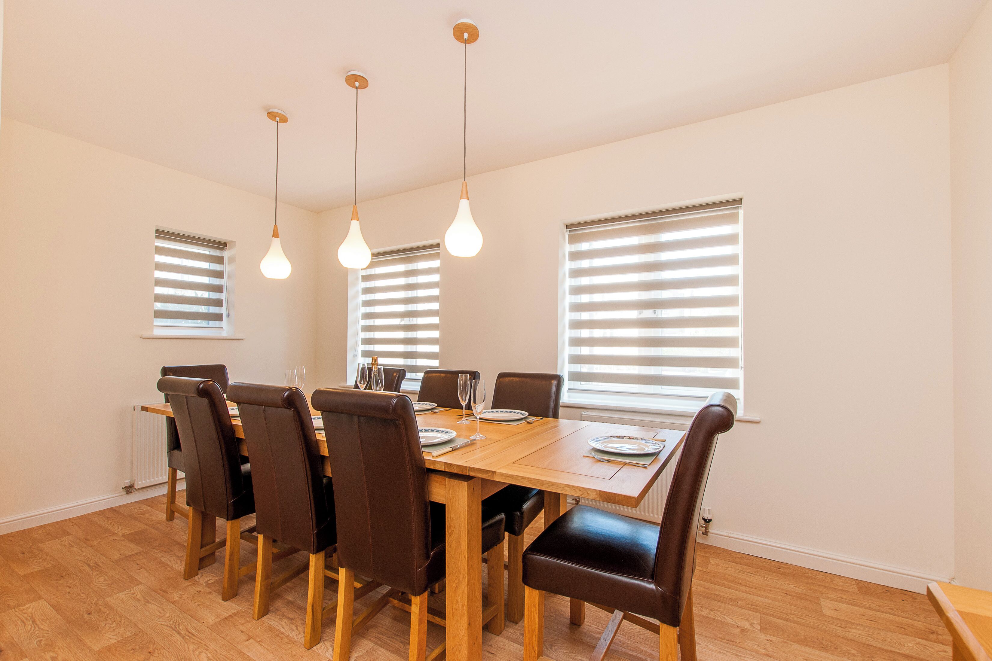 A dining area with a wooden table, six chairs, and hanging light fixtures.