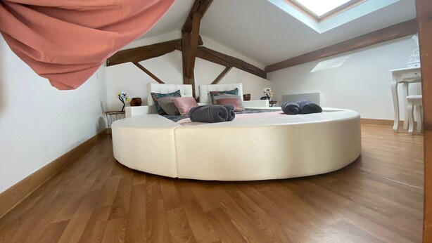 A circular bed in a room with wooden beams, a skylight, and a white table with chairs.