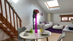 A modern living room with a dining area, wooden staircase, and skylights.
