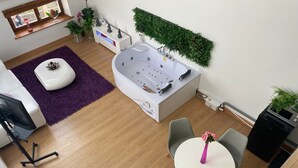 A modern bathroom with a large bathtub, a small table with chairs, and a window with plants.