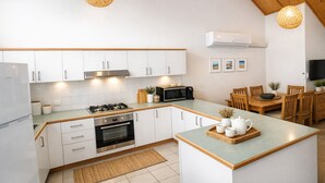 Una cucina moderna con mobili bianchi, un'isola centrale, un'area pranzo con sedie di legno e due lampade a sospensione.