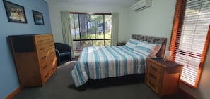 Relax in this cozy space with a large bed, dresser, and chair, plus a window with curtains for natural light.