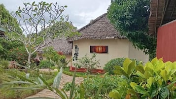 Une maison traditionnelle avec un toit de chaume, entourée d’une végétation luxuriante et bordée d’un sentier en pierre.