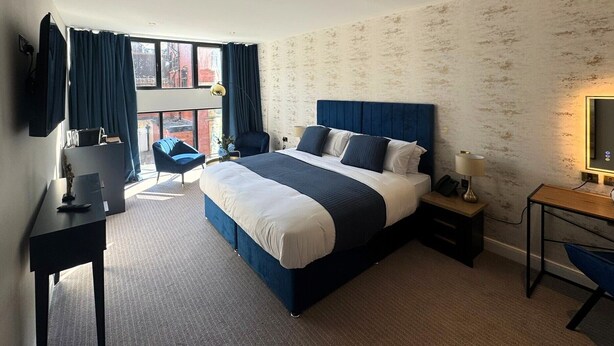 Quarto de hotel com uma cama grande, uma mesa, uma cadeira e vista da cidade pela janela.