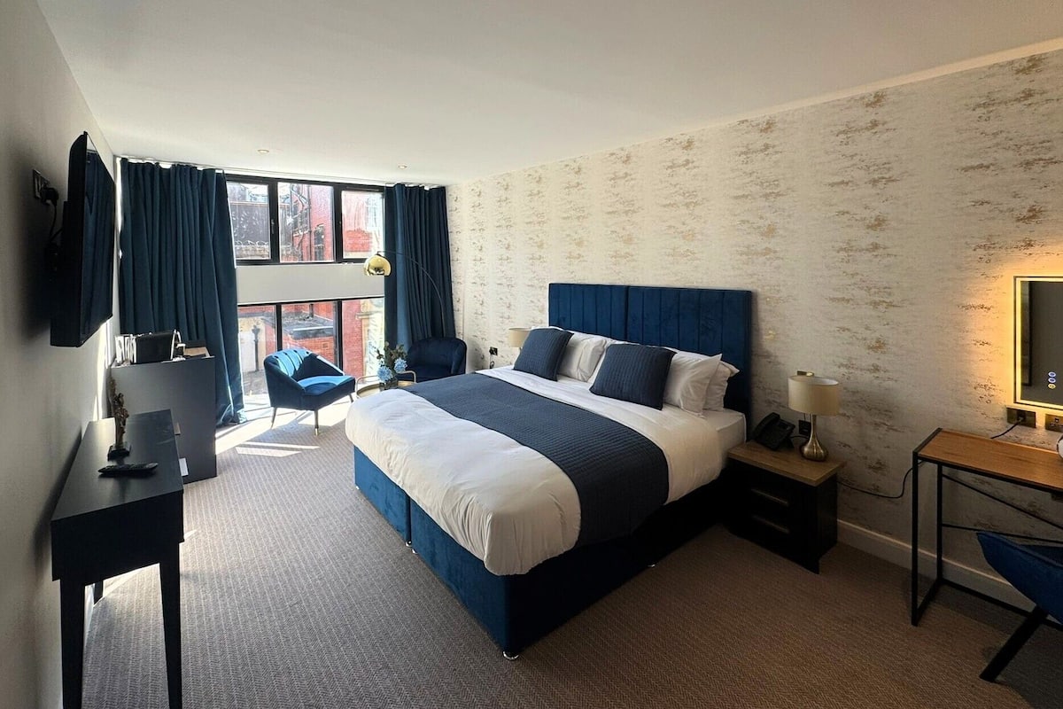 A hotel room with a large bed, a desk, a chair, and a view of the city through the window.