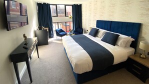 Quarto de hotel com uma cama grande, uma escrivaninha, uma cadeira e uma televisão.
